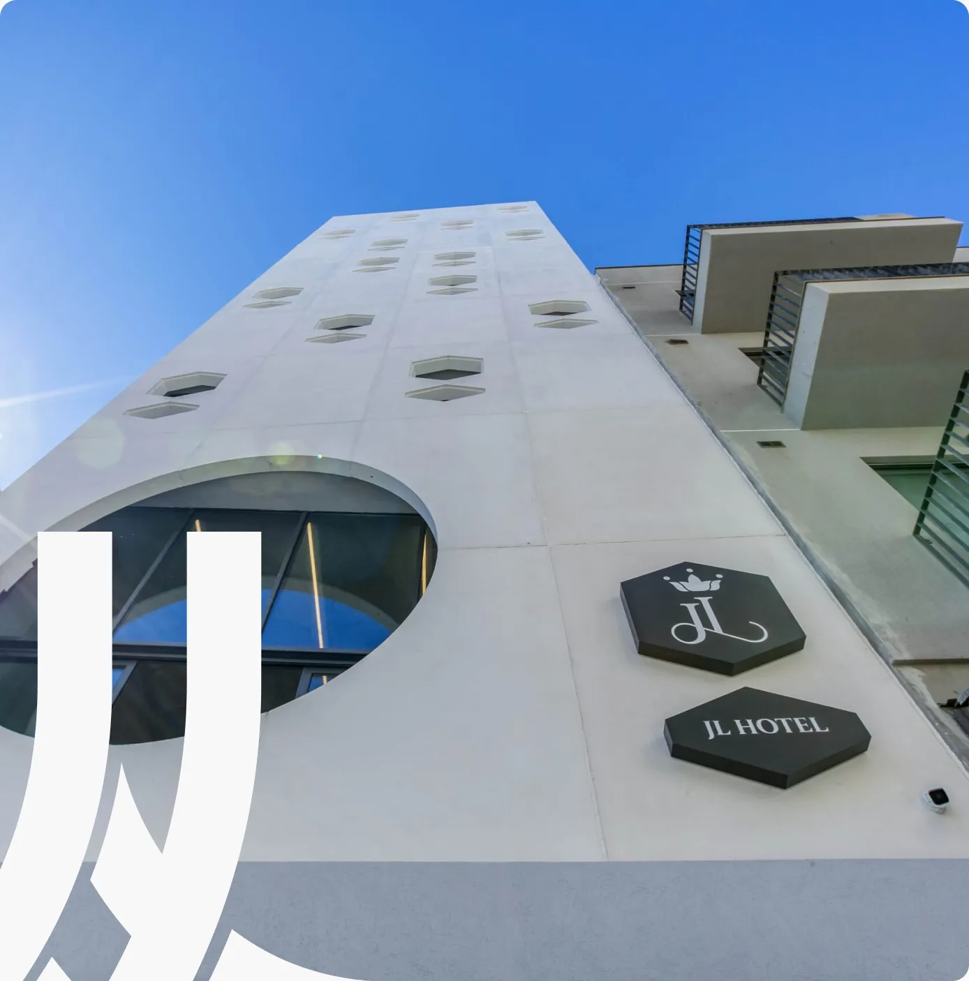 The white facade of JL Hotel with its hexagonal signage against a blue sky