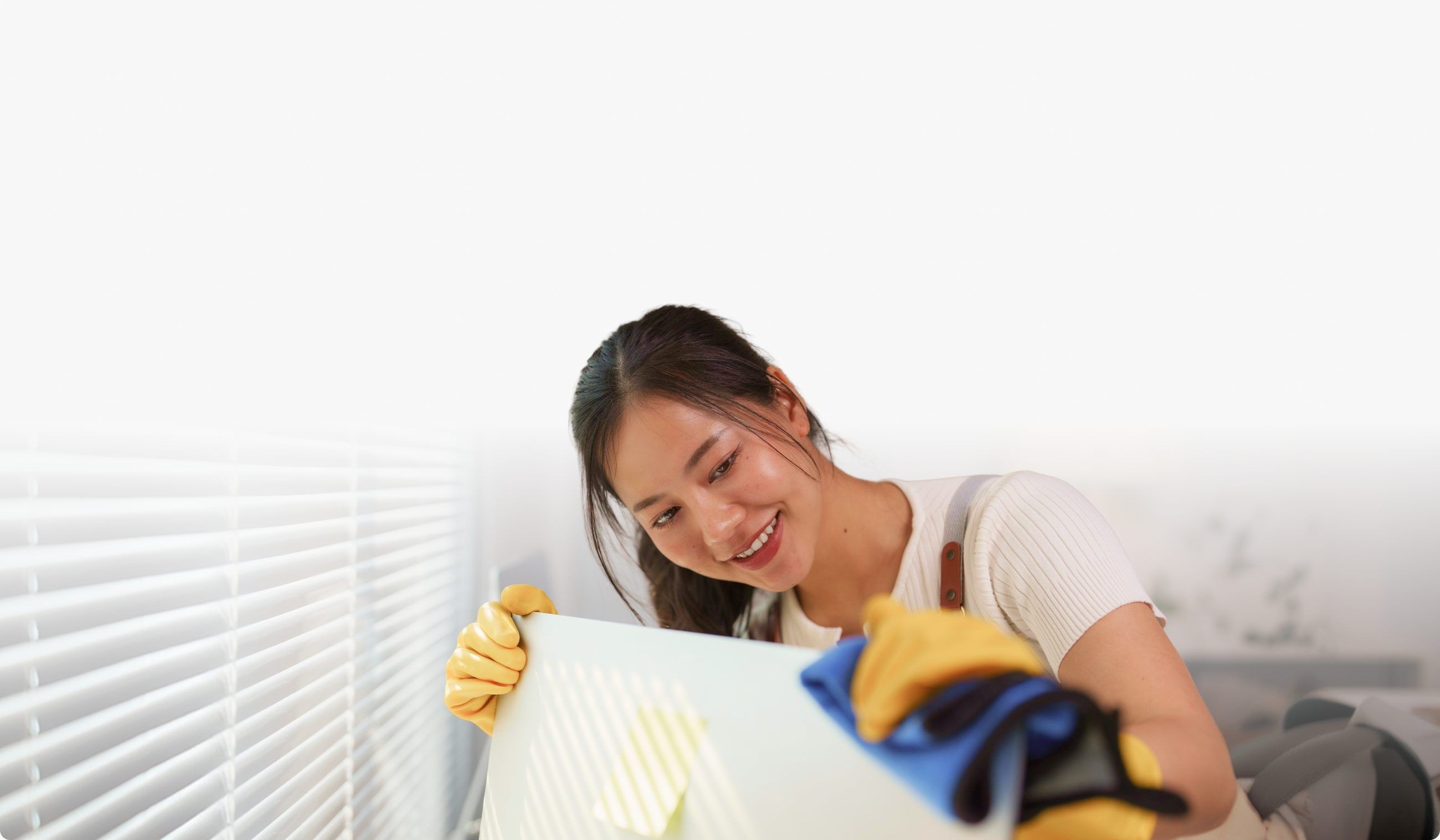 A smiling cleaner in yellow gloves wiping down a white surface