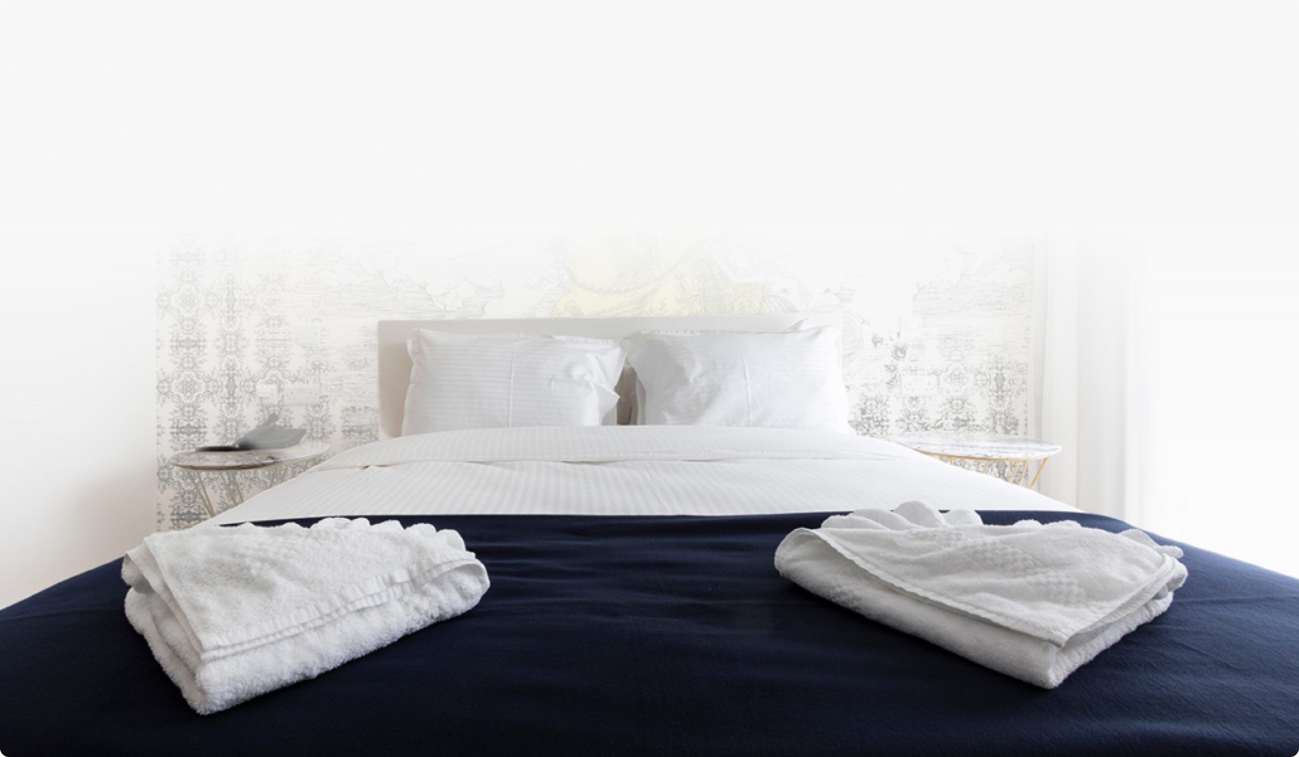 A made-up hotel bed with folded white towels on a navy throw
